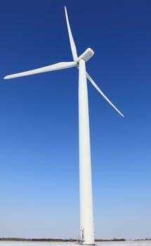 Wind turbine in a field covered by sbow in winter.There is a little motion blur at the tips of the blades.