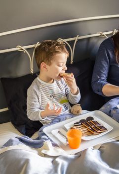 Happy mother and son having breakfast in bed at home in the morning