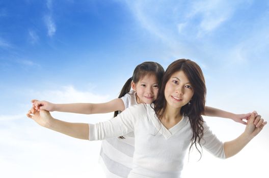 Happy Asian mother piggyback ride daughter over blue sky