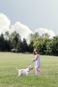 A happy little girl walks her puppy, an English Cream Labrador Retriever - Golden Retriever mixed designer breed, on a beautiful spring day. Extreme shallow depth of field.
