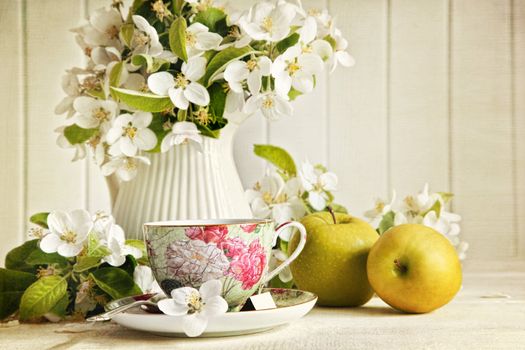 Tea cup with fresh flower blossoms and green apples