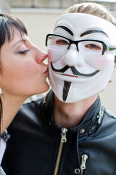 Woman kissing man in vendetta mask in glasses.