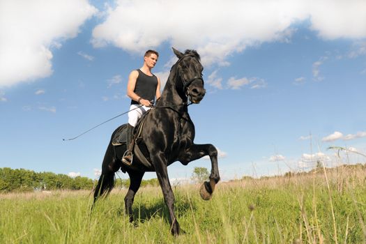 young man and his black stallion in  a field