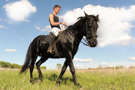 young man and his black stallion in  a field