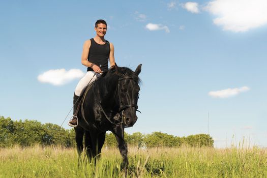 young man and his black stallion in  a field