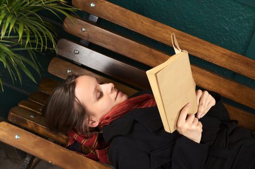 Young Caucasian woman lying on a bench reading a book (Selective Focus, Focus on the right eye) 
