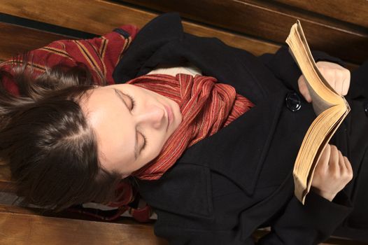 Young Caucasian woman lying on a bench reading a book (Selective Focus, Focus on the eyes) 