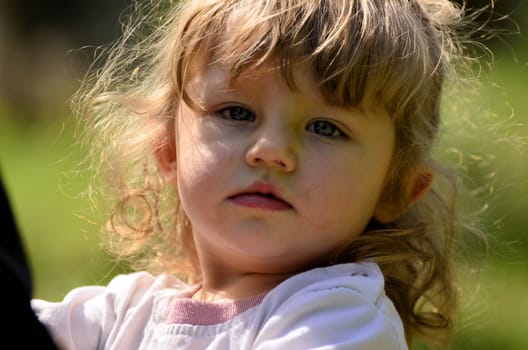 The photo shows a close-up of a happy, littlel girl during her playing with her sister in the park.