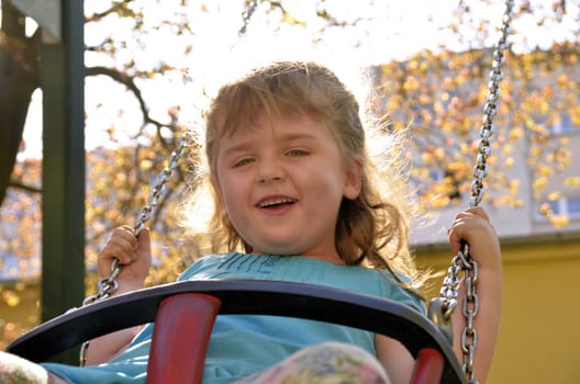 The photo shows a happy, smiling and joyful girl during her playing on the swing.