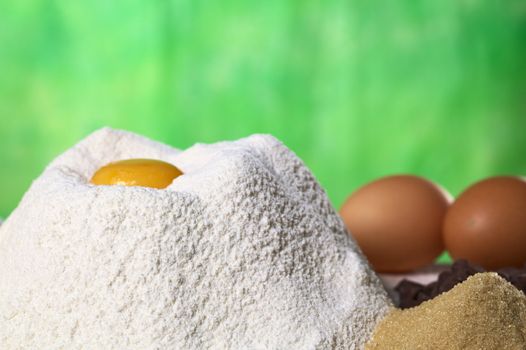 Flour with egg yolk in the middle surrounded by brown sugar, chocolate chips and eggs (Selective Focus, Focus on the front of the flour pile)