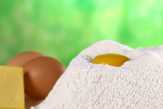 Flour with egg yolk in the middle surrounded with butter and eggs on the side (Selective Focus, Focus on the upper front edge of the flour pile)