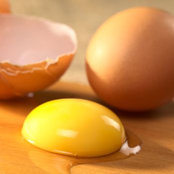 Raw egg yolk and egg white with the cracked open egg shell and a complete egg in the back (Selective Focus, Focus on the front of the egg yolk)