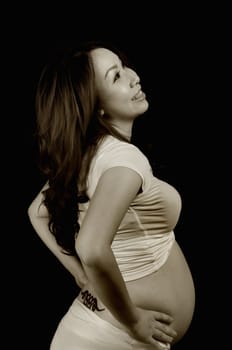 Asian pregnant lady standing on black background, sepia tone.