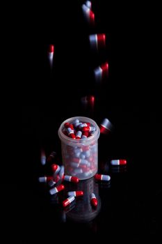 Filling a container already full of capsules - isolated on black background