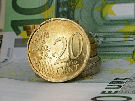 20 cent  coin over pile of other coins on a one hundred euro banknote
