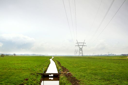 Dutch typical rural flat landscape with channel and high-voltage line 