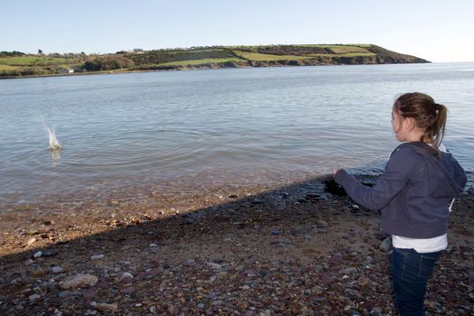 young girl throwing stones from the shore into the sea