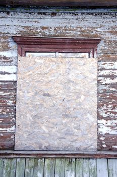 Abandoned grunge village house window nailed-up with wood chipboard. Ancient architecture background.