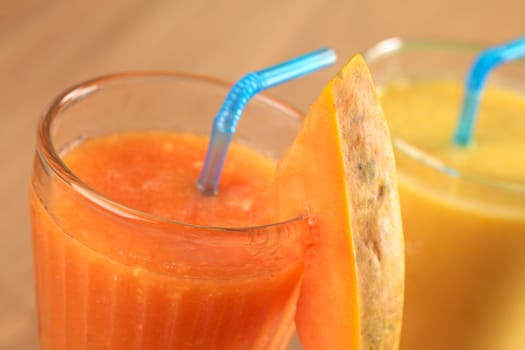 Fresh papaya juice garnished with a papaya slice, mango juice in the back (Selective Focus, Focus on the upper edge of the papaya slice and the front rim of the glass)