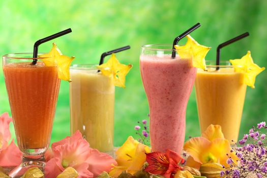 Fresh papaya, strawberry, pineapple and mango fruit juices and milkshakes decorated with flowers (Selective Focus, Focus on the papaya and strawberry juices in the front)