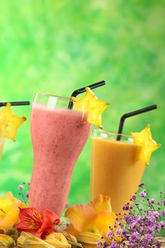Strawberry and mango milkshakes garnished with carambola slice surrounded by flowers (Selective Focus, Focus on the front of the strawberry milkshake and the carambola garnish)