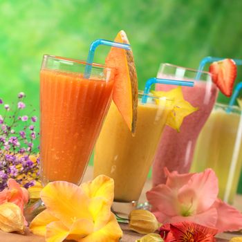 Fresh papaya, mango, strawberry and pineapple fruit juices and milkshakes decorated with flowers (Selective Focus, Focus on the papaya juice and the papaya slice garnish)