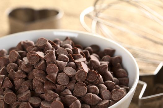 Chocolate chips surrounded by baking utensils (beater and cutters) (Selective Focus, Focus on the chocolate chips on top and the ones in the same plane)