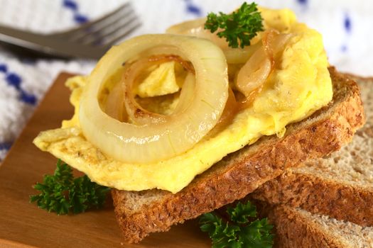 Scrambled eggs open sandwich with fried onions and fresh parsley leaves (Selective Focus, Focus on the front of the egg and the onion)