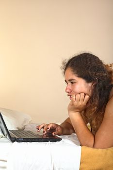 Young Peruvian woman with laptop lying on bed (Selective Focus, Focus on the left eye of the woman)