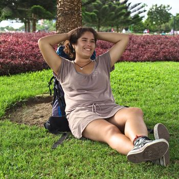 Young Peruvian woman with backpack leaning against a tree in a park in Miraflores, Lima, Peru (Selective Focus, Focus on the face of the woman)