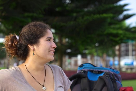 Young smiling Peruvian woman with backpack in park (Selective Focus, Focus on the face of the woman)