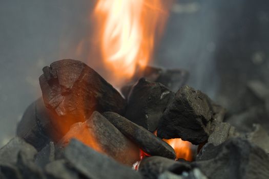 Burning charcoal with orange-colored flame and smoke (Selective Focus, Focus on the front of the big charcoal piece on the left side of the flame)