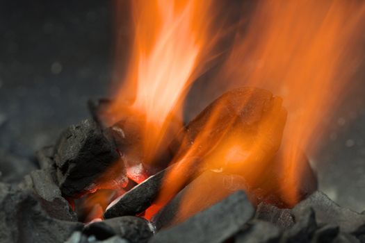 Burning charcoal with orange-colored flame and glow (Selective Focus, Focus on the front of the charcoal piece on the left side of the flame and on the one in the flame)