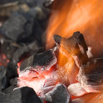 Burning charcoal with orange-colored flame and glow (Selective Focus, Focus on parts of the charcoal pieces around the flame)