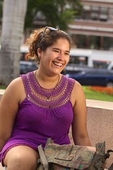 Beautiful smiling young Peruvian woman in purple dress sitting in park in Lima, Peru (Selective Focus, Focus on the face of the woman) 