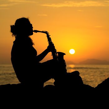 The silhouette of a young female musician playing her saxophone on the coast at sunset