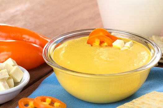 Peruvian Huancaina Sauce (spicy cheese sauce) made of cheese, soda crackers, aji (Peruvian yellow chili pepper) and milk in a glass bowl (Selective Focus, Focus on the front of the aji slices and the cheese on the sauce) 