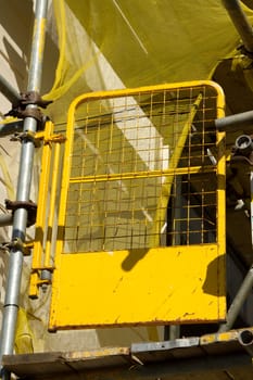 A yellow safety gate on a scaffold structure with yellow netting.