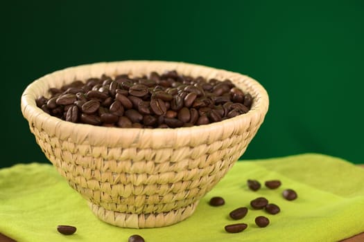 Roasted coffee beans in woven basket with green background (Selective Focus, Focus on the coffee beans in the middle of the basket)
