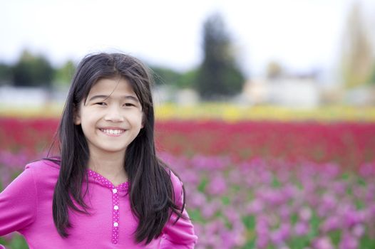 Biracial ten year old girl happily standing in front of tulip field. “Courtesy of RoozenGaarde (Tulips.com).”