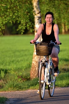 The picture shows the young woman on a bicycle rides along the birch alley.