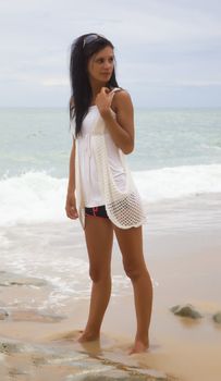 Slim brunette on a beach in a white dress against a background of sea waves