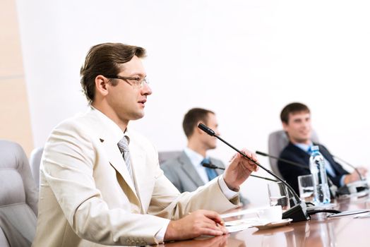 Portrait of a businessman, said into the microphone, in the background colleagues communicate with each other