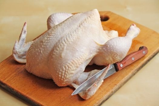 Whole raw chicken on the chopping board with a knife
