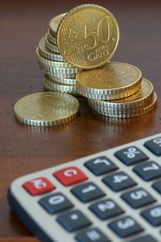 A stack of 50 cents euro coins and a calculator. Focus on currencies.