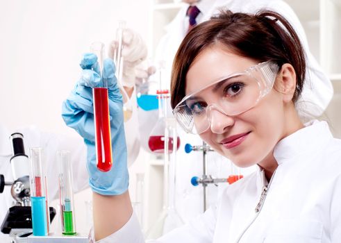 portrait of a beautiful woman chemist, looks at a test tube with red fluid