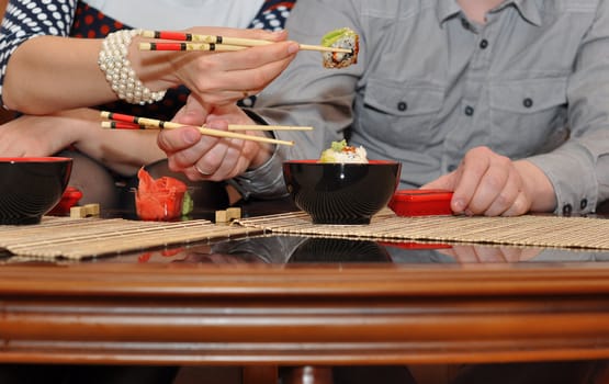 Male and female hands with sticks and sushi