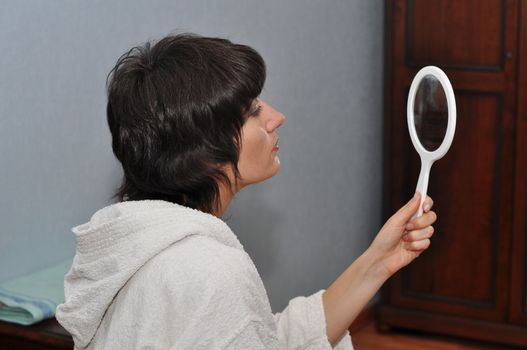 Young woman looking in the white hand mirror