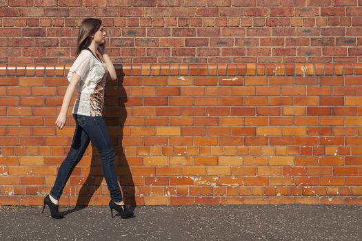 Young woman walk beside the red brick wall while  talking on the phone