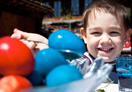 Happy little boy smiling behind blue and red coloured easter eggs, focus on kid